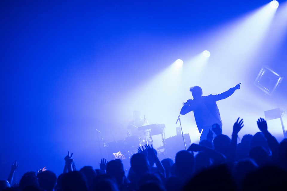 A crowd with raised hands under blue stage lights